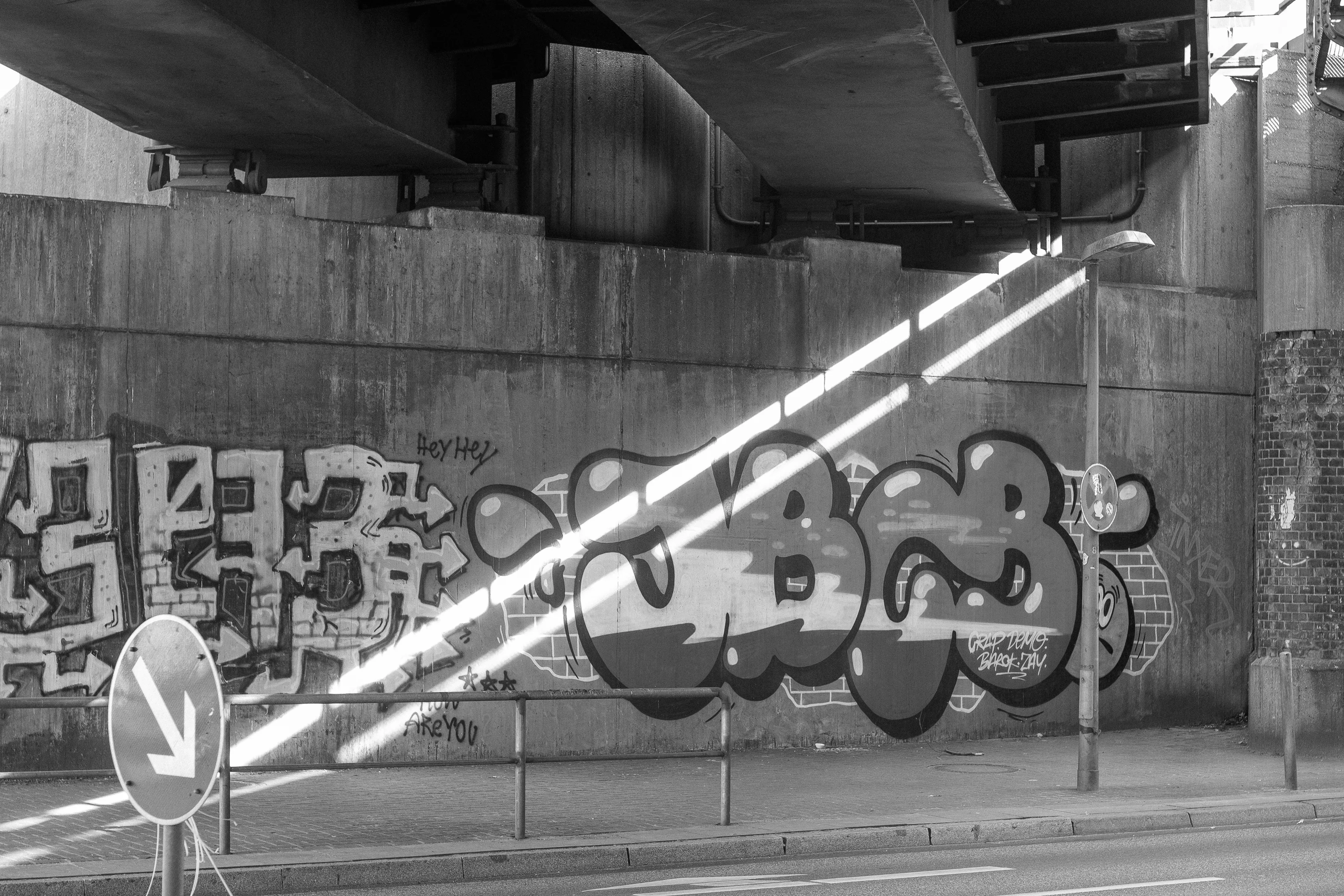 Graffiti on a concrete wall under a bridge with sunlight streaming in diagonally.