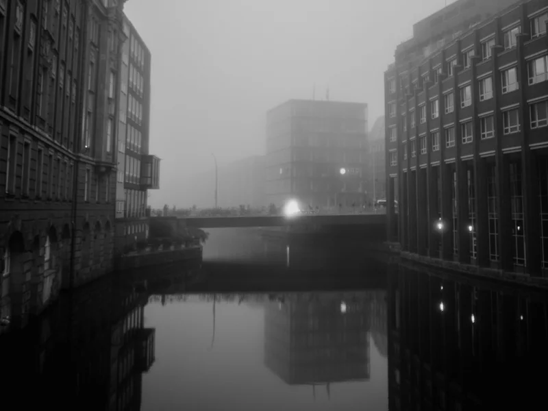 Foggy cityscape with buildings and their reflections in a canal.