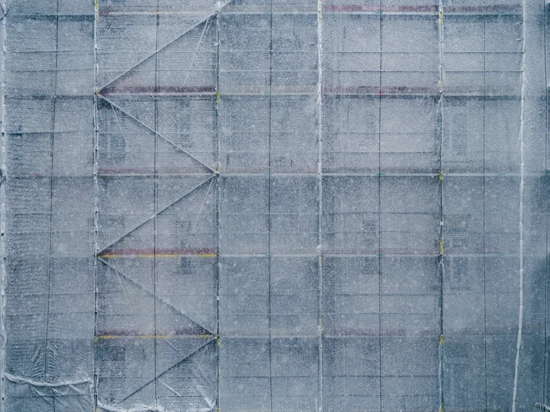 Scaffolding covered in protective netting with visible diagonal bracing patterns.