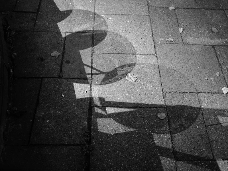 Shadows of circular stools cast on a paved sidewalk.