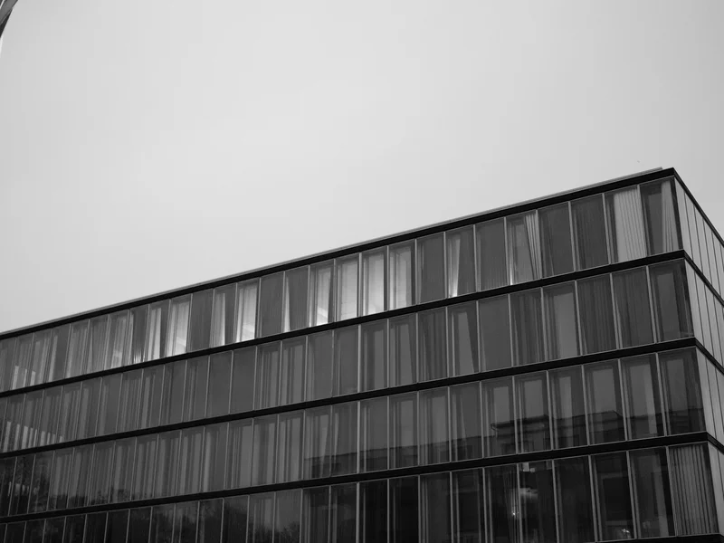 Black and white image of a modern glass building facade against a clear sky.