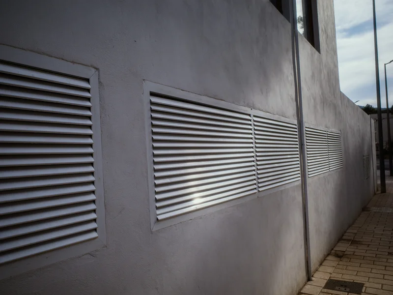 Exterior wall with three horizontal ventilation grilles and a vertical pipe.