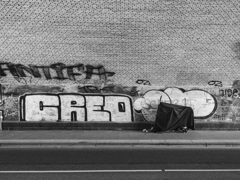 Black and white graffiti on a brick wall above a covered object on the sidewalk.