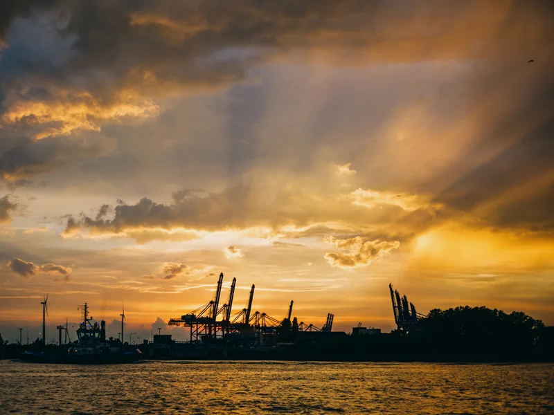 Harbor cranes silhouetted against a dramatic sunset sky.