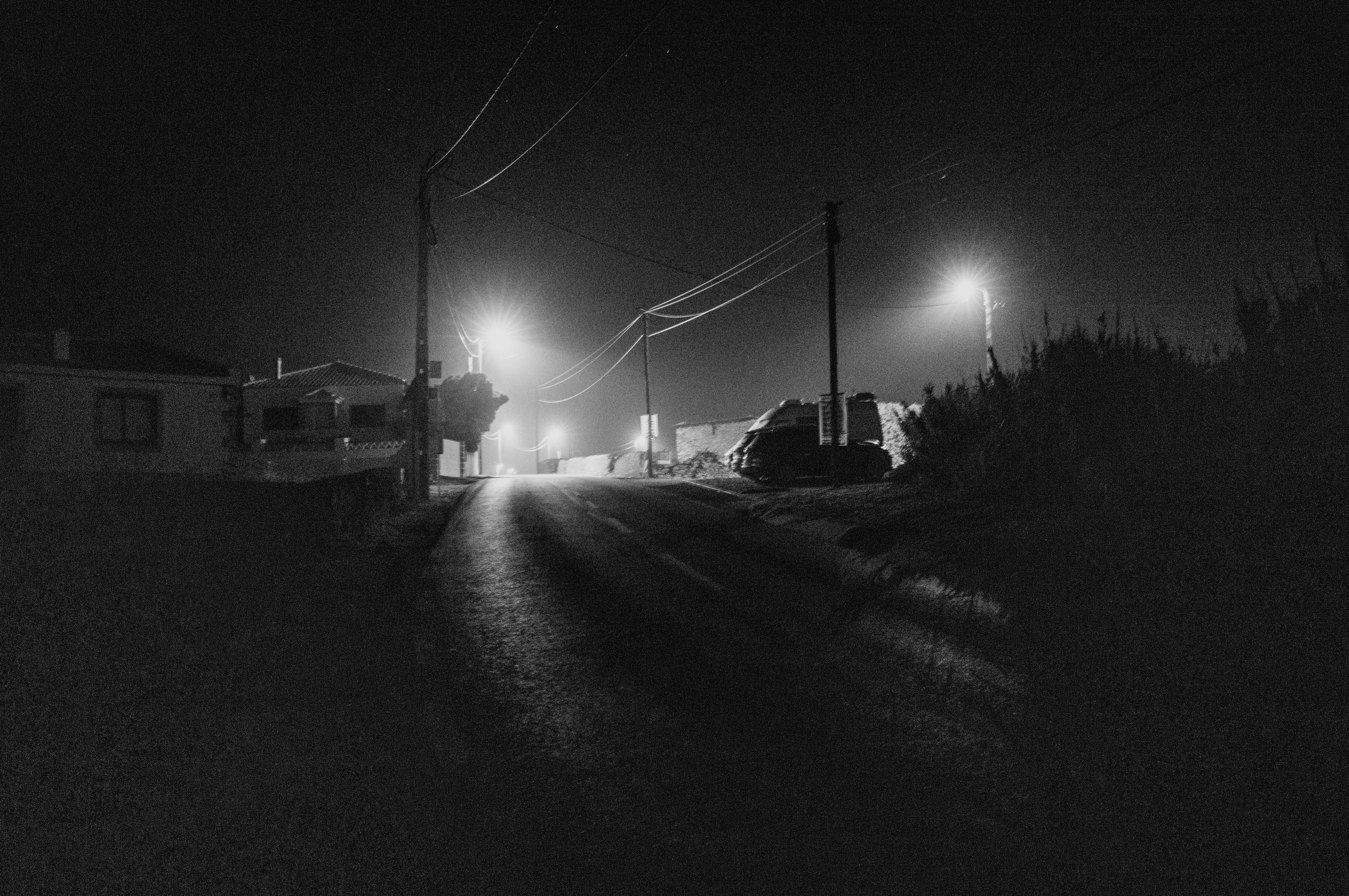 A nighttime street scene with streetlights illuminating a quiet road and silhouetted buildings.