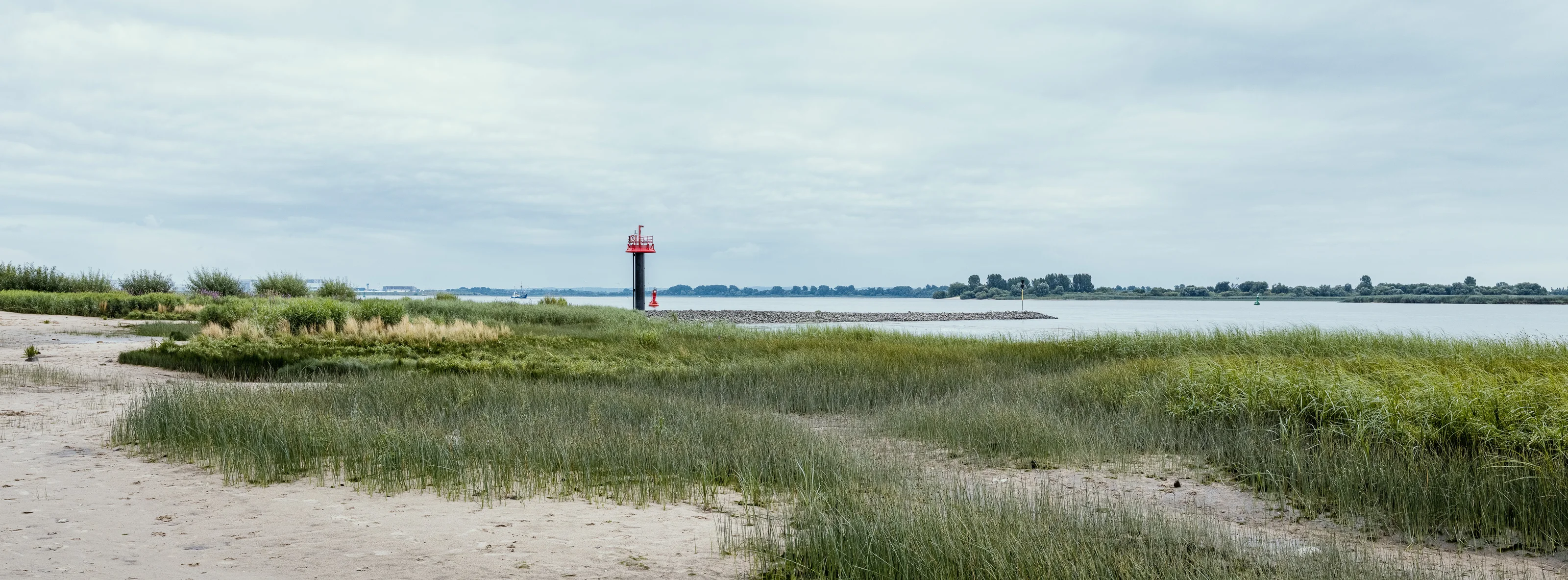 A scenic coastal landscape with a red lighthouse by the water's edge.