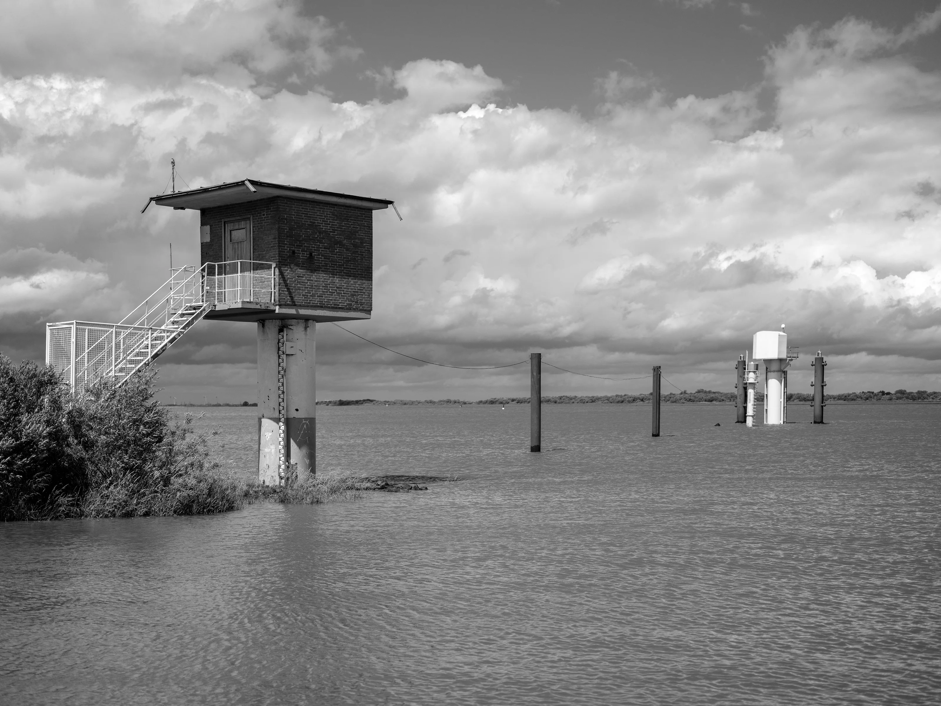 A water monitoring station elevated on a platform above water with a cloudy sky.
