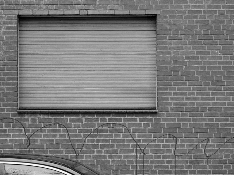 A closed roll-up shutter on a brick wall with the top of a car visible in the foreground.