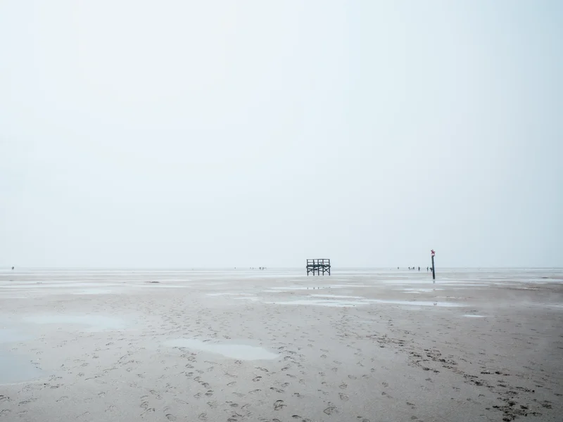 A vast, empty beach with a distant lifeguard stand and calm ocean in the background.