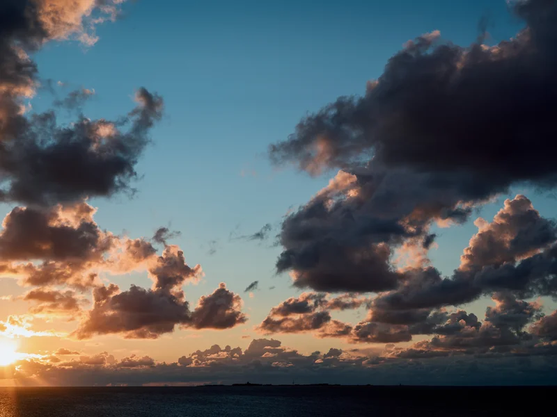 Sunset over the ocean with dramatic clouds and a glowing horizon.