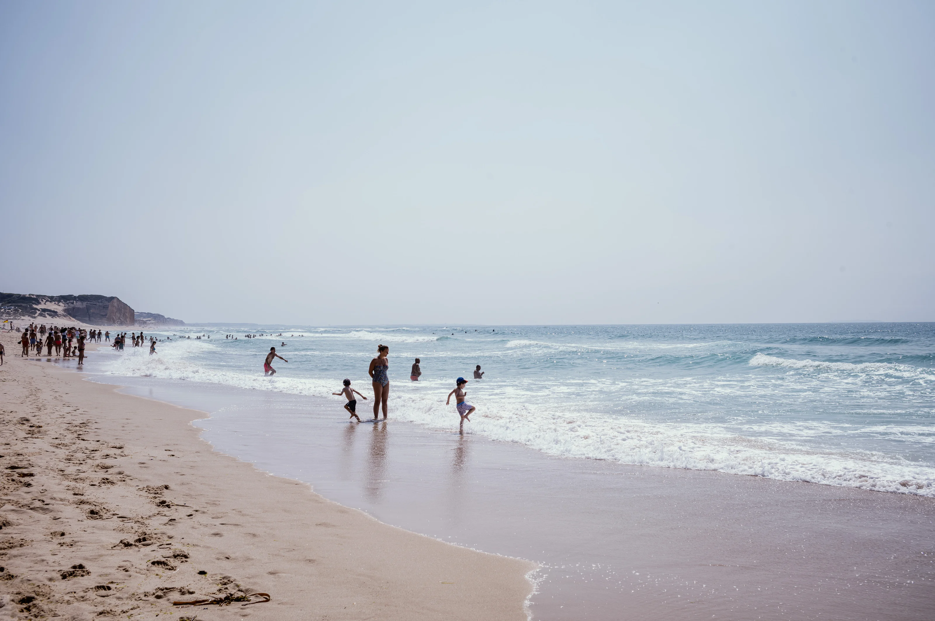 People enjoying a sunny day at the beach with waves in the background.
