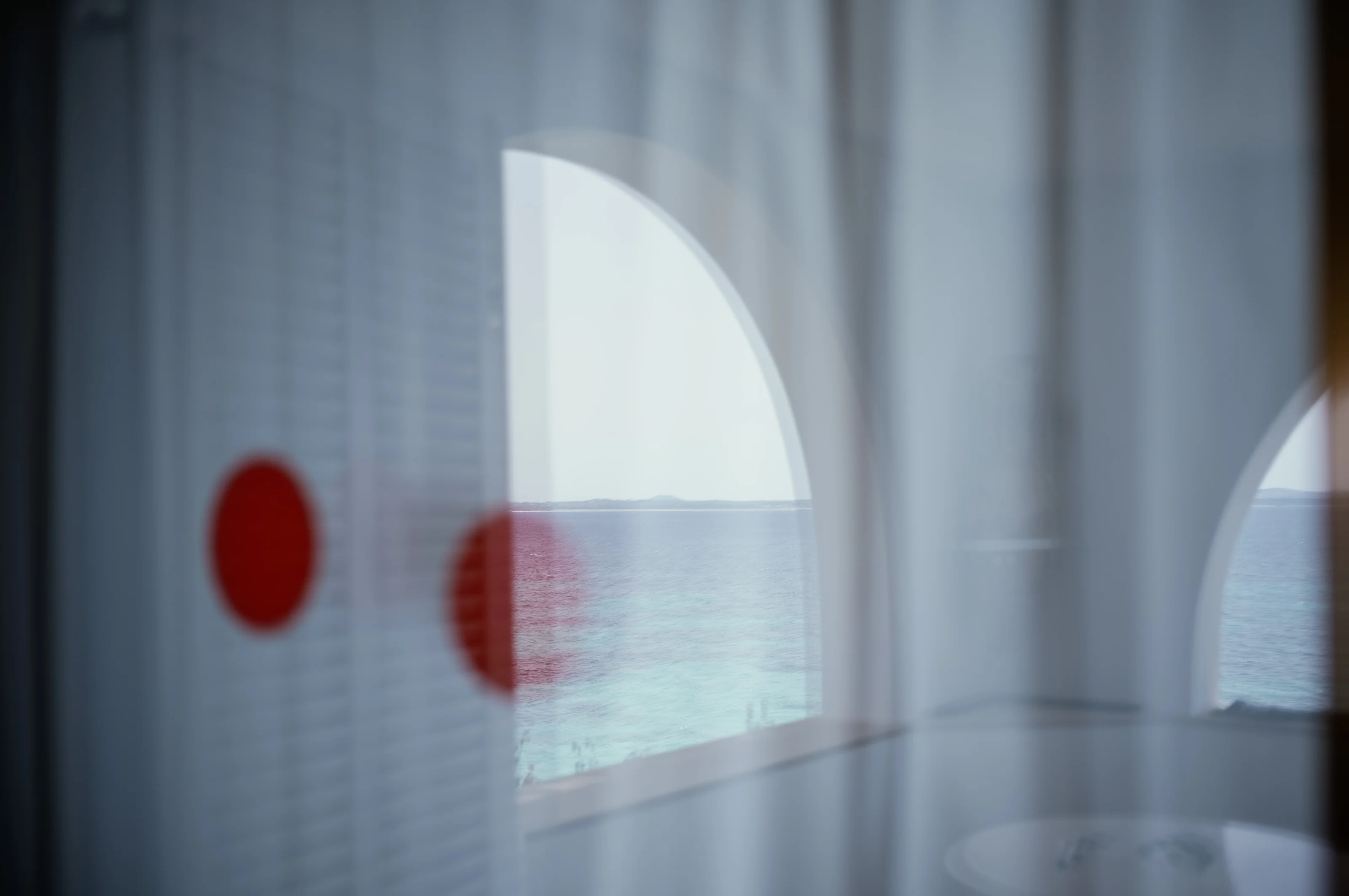 View through a window with reflections of red dots and a sea horizon visible outside.