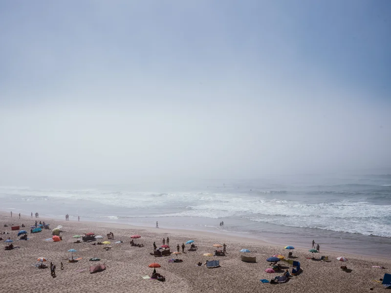 A foggy beach with several umbrellas and people scattered along the shore.
