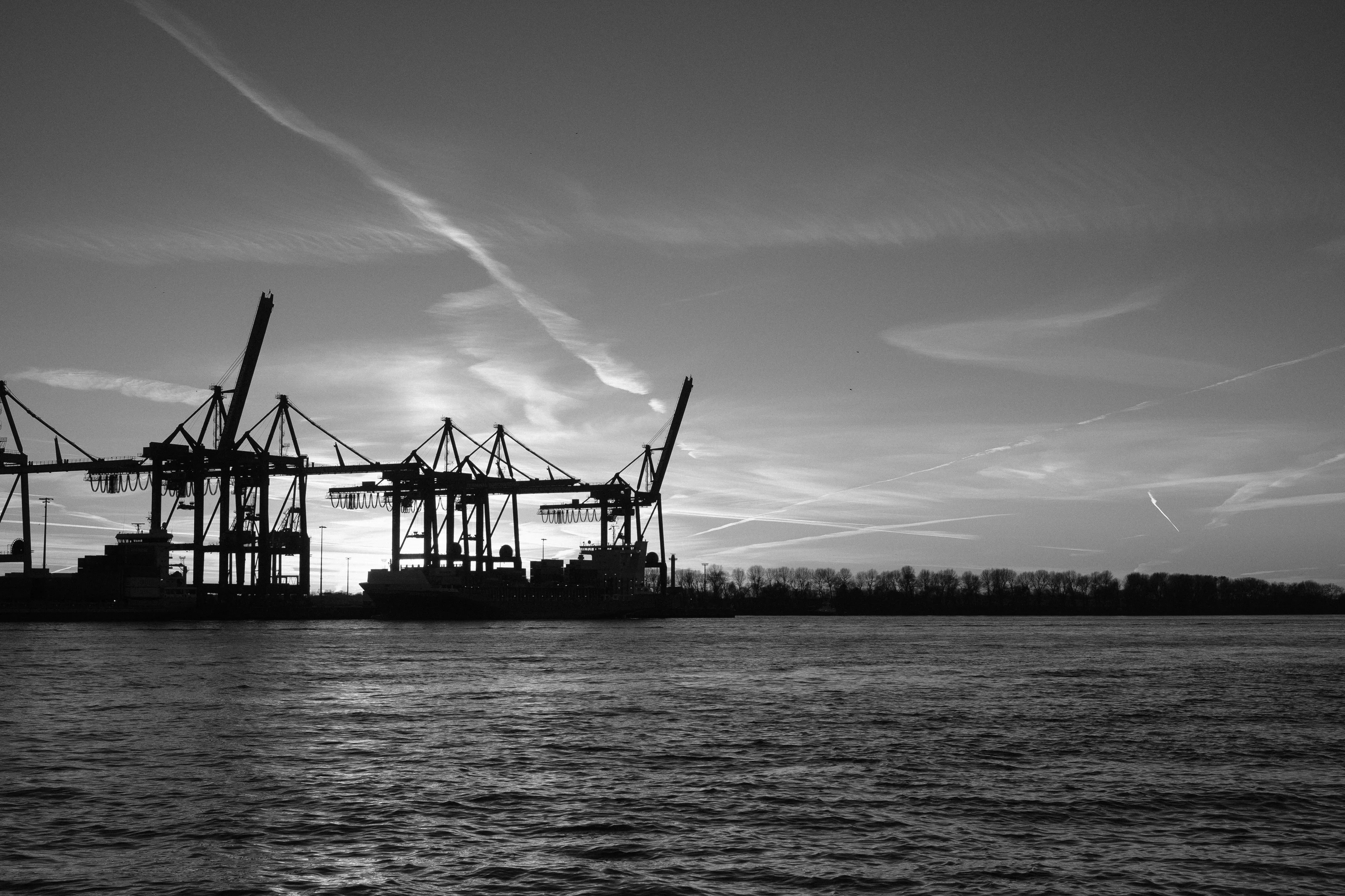 Silhouette of cargo cranes at a port against a dramatic sunset sky.