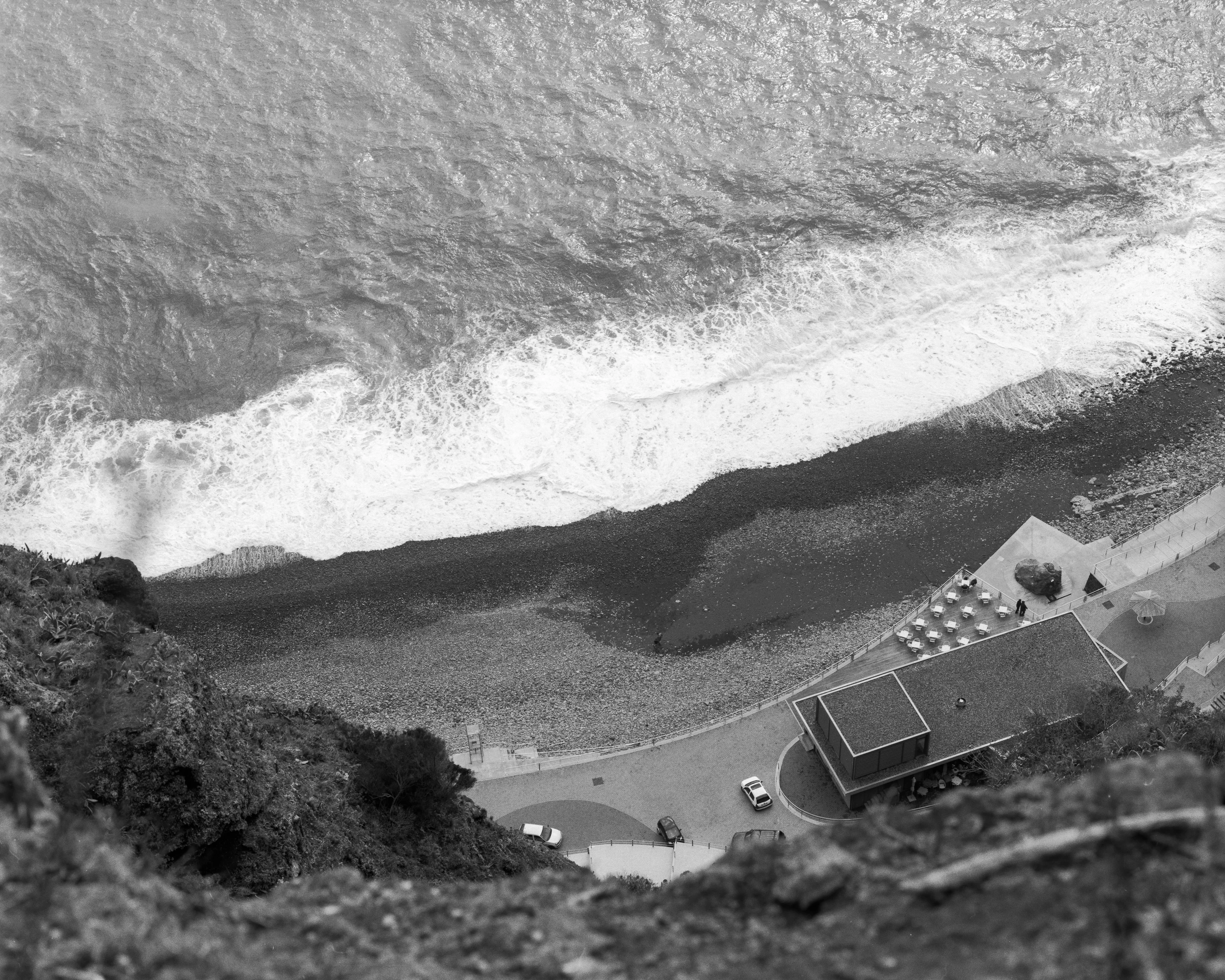 Aerial view of a coastline with waves, a pebble beach, and a nearby building.