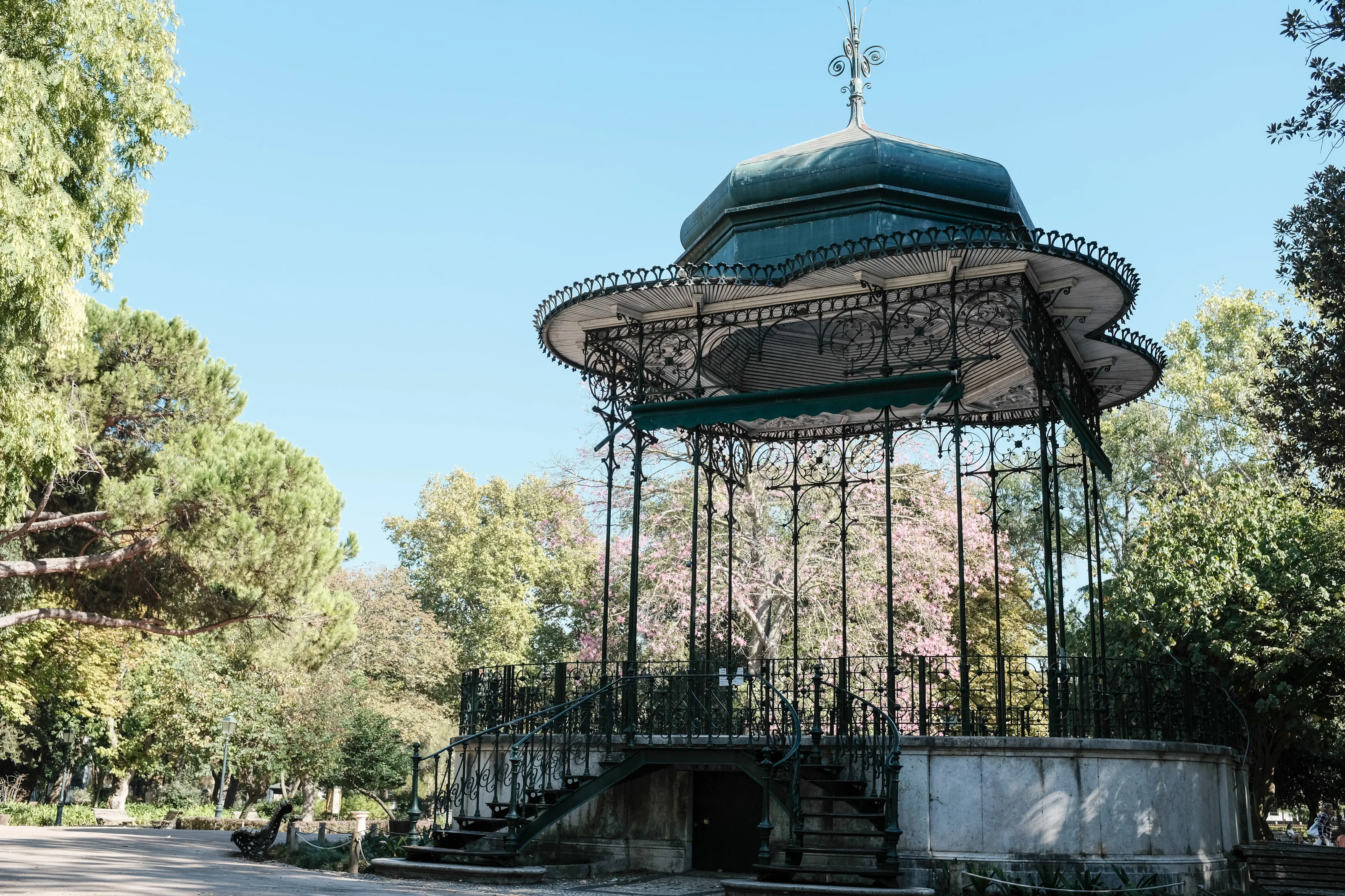 An ornate bandstand with intricate wrought iron details in a park setting.