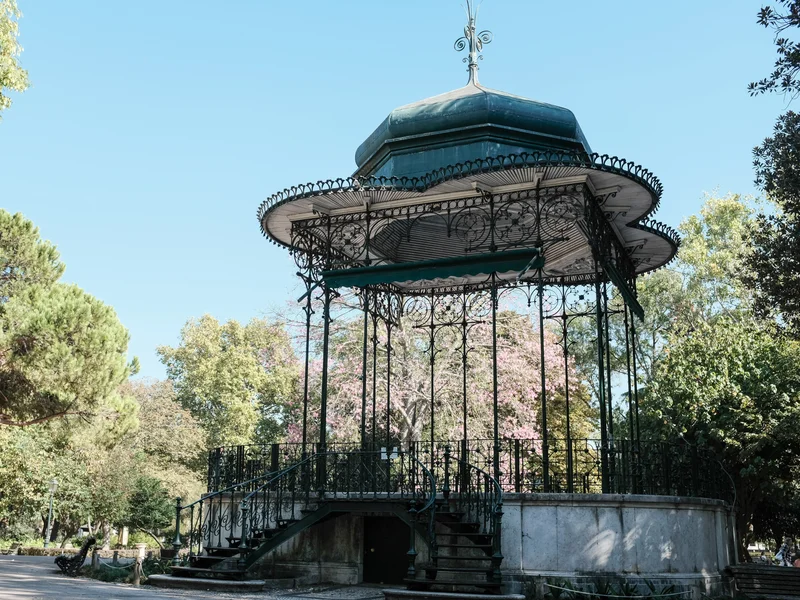 An ornate bandstand with intricate wrought iron details in a park setting.