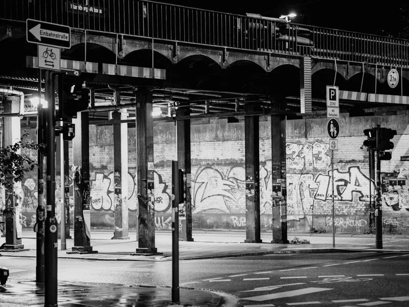 Black and white urban scene with graffiti-covered walls under an overpass at night.