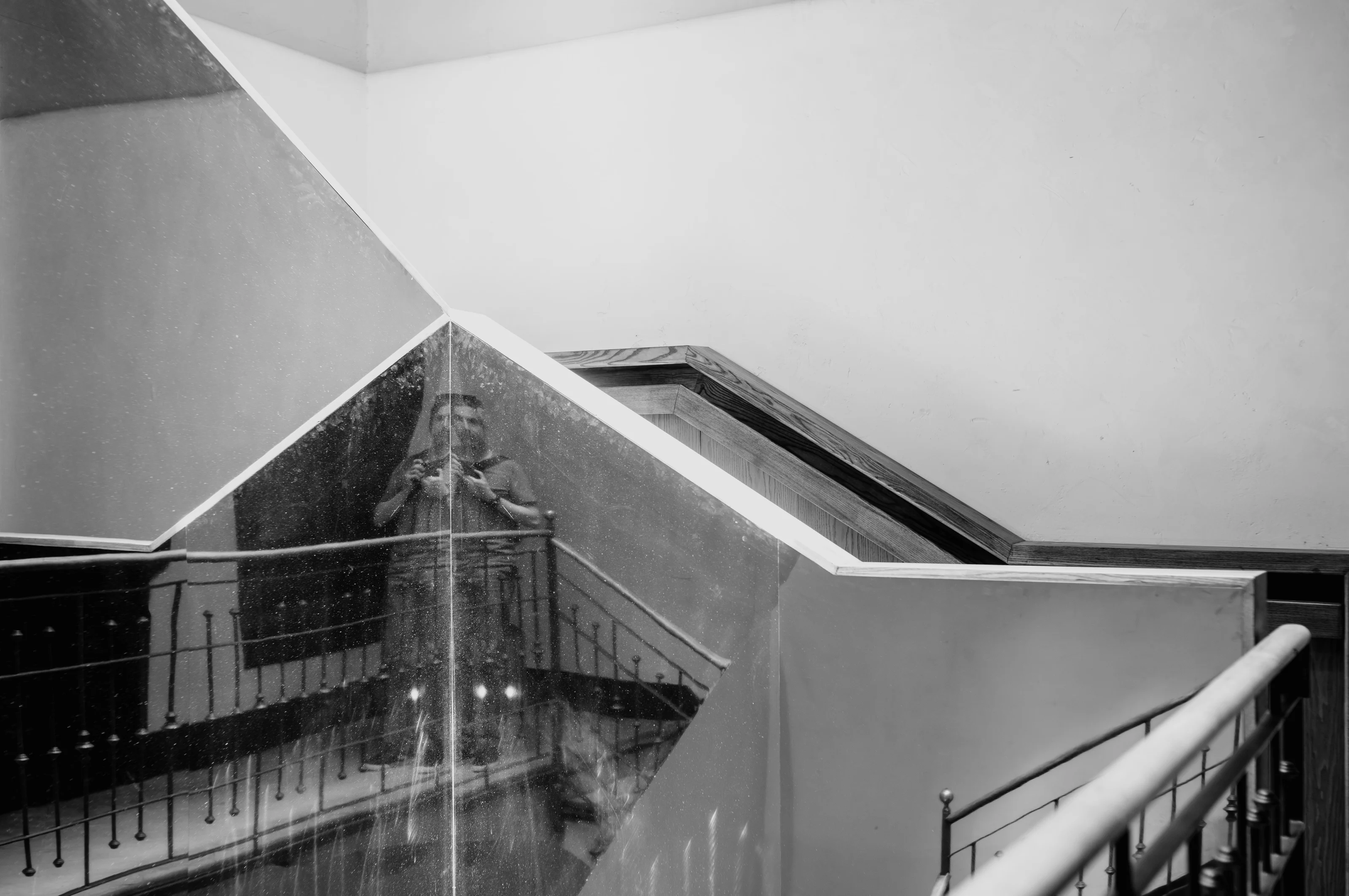 Person taking a photo reflected in a complex, geometric mirror on a staircase.