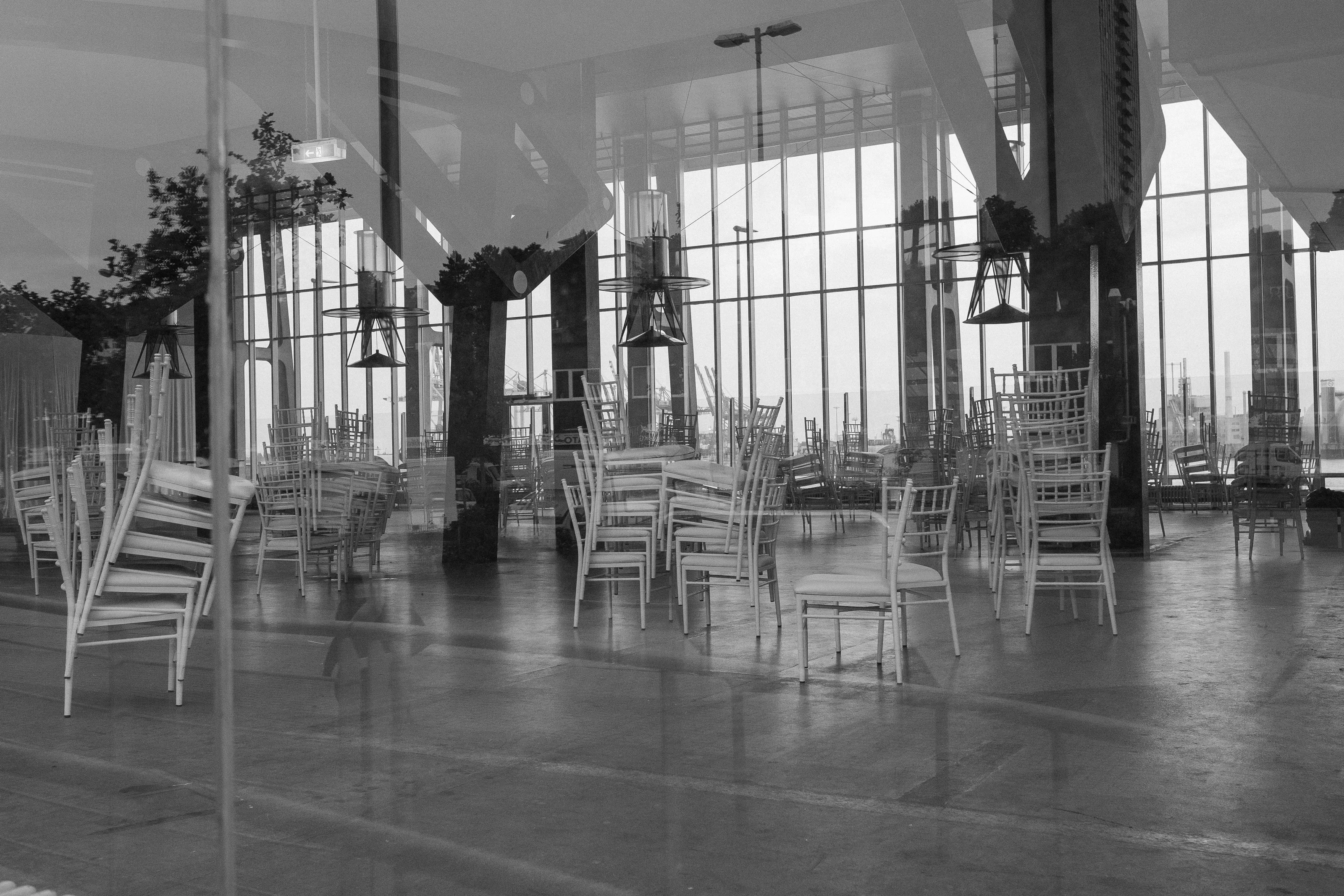 A black and white image of stacked chairs inside a room with large windows.