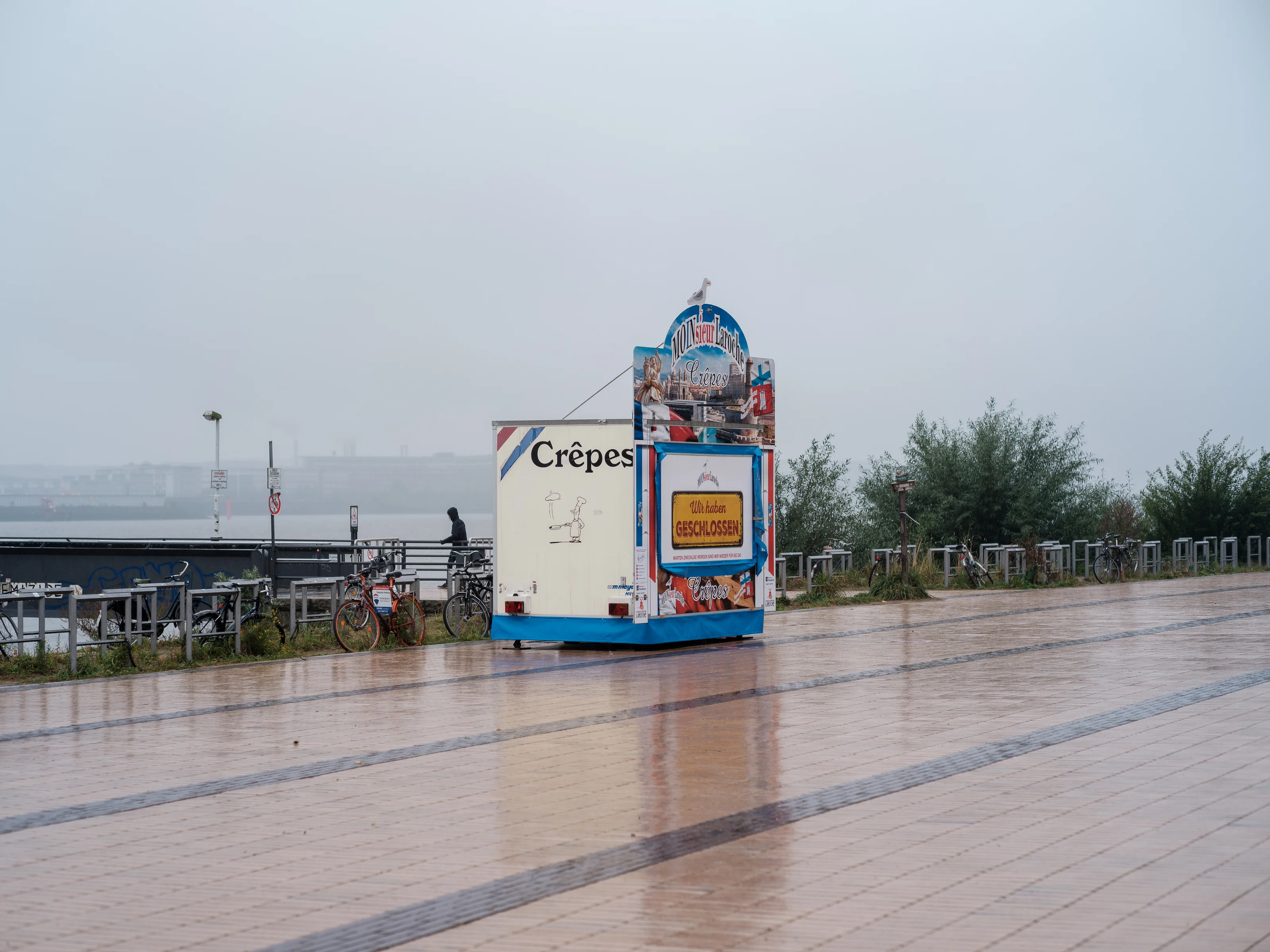 A closed crepe stall on a rainy boardwalk with bicycles nearby.
