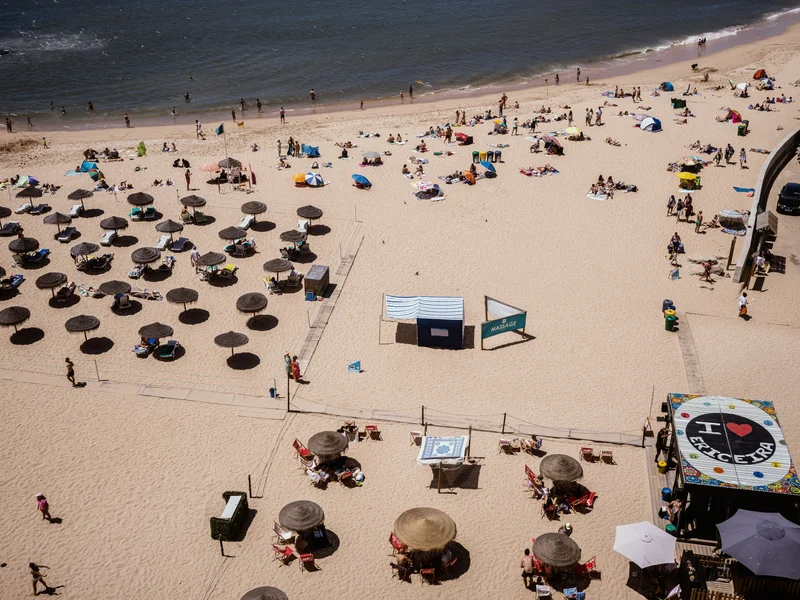 Aerial view of a sandy beach with umbrellas, sunbathers, and a massage tent.