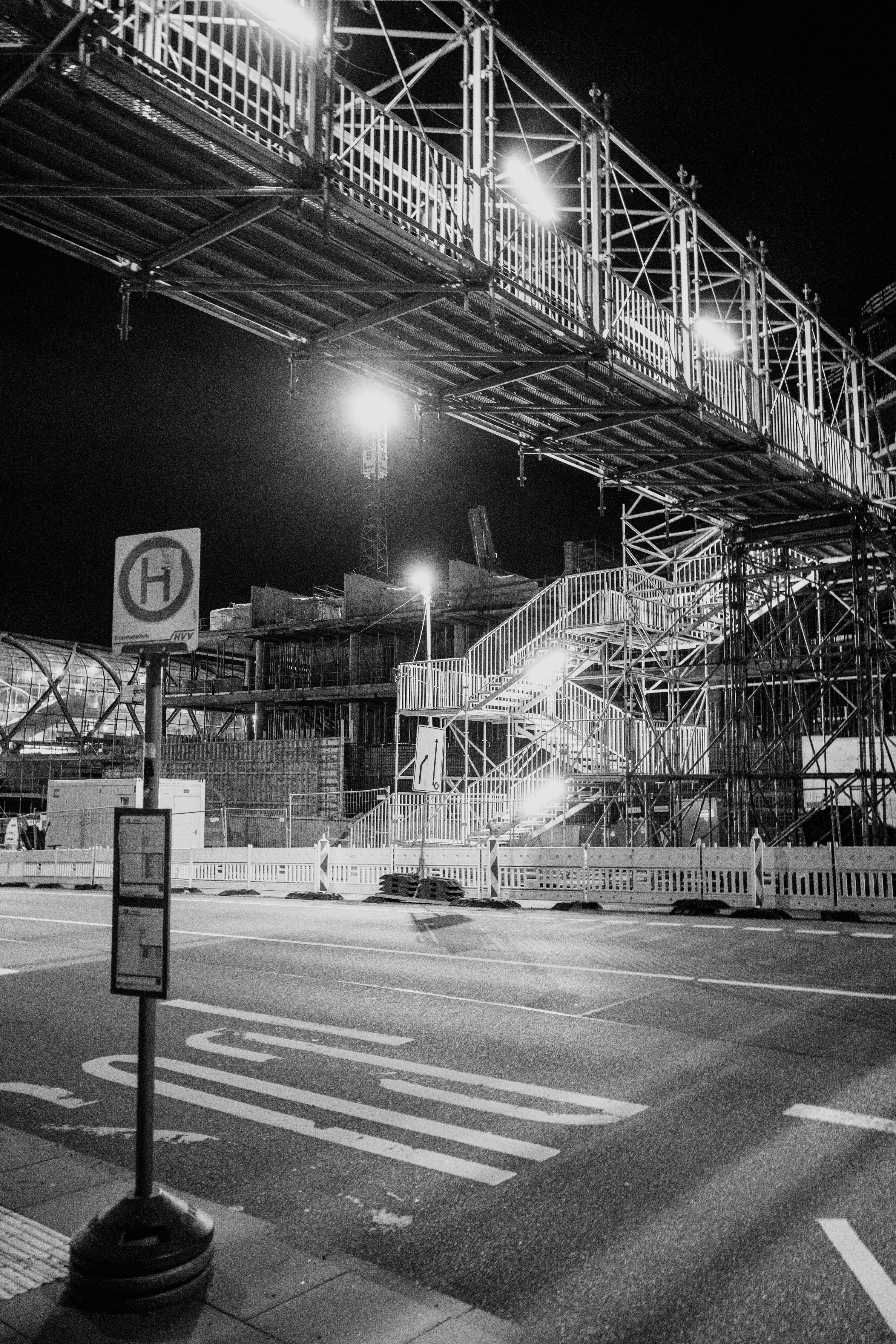 A night scene showing a construction site with illuminated scaffolding and an overpass.