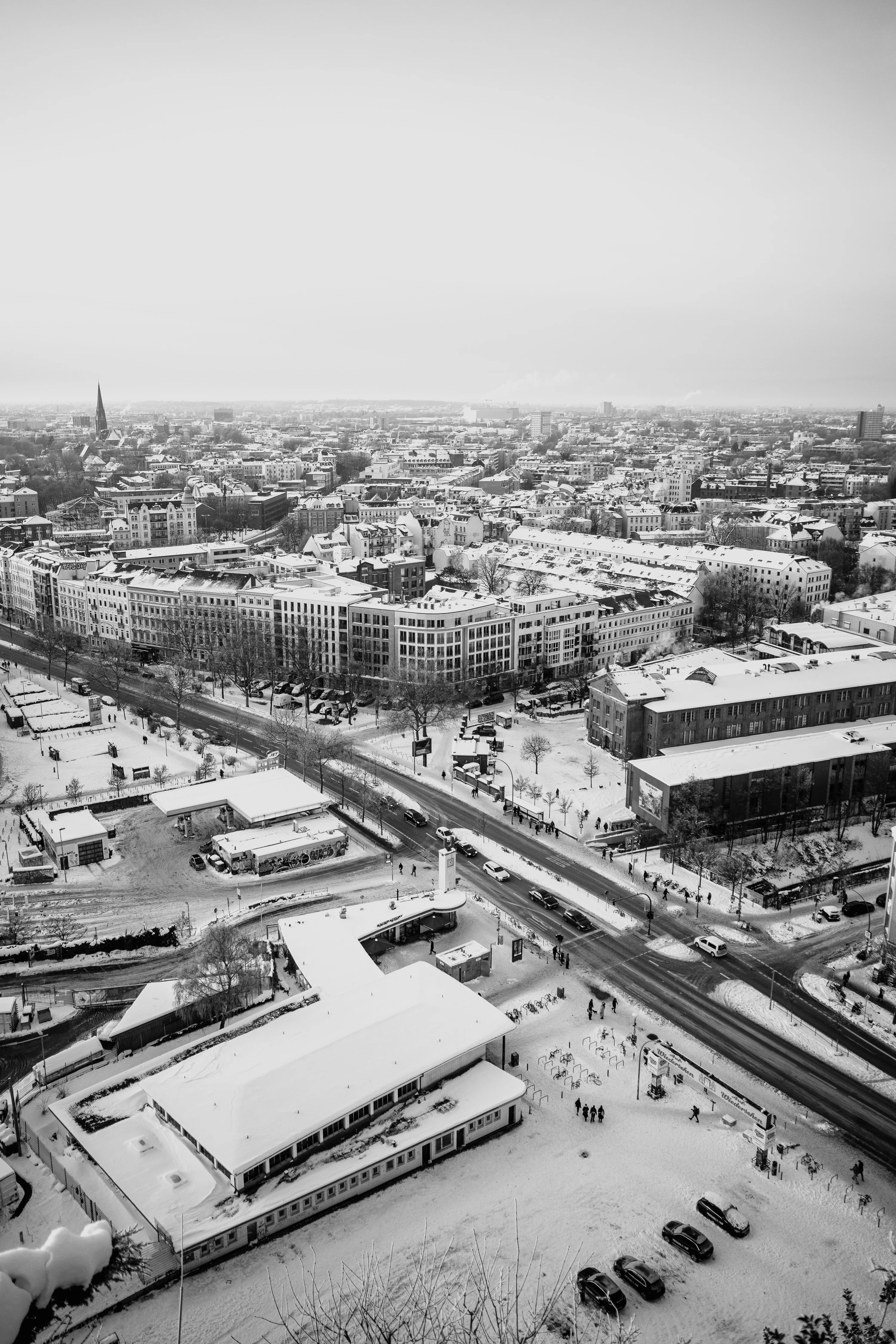 A snowy urban cityscape captured from above, showing buildings, roads, and vehicles.