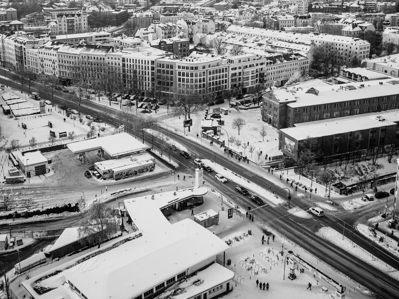 A snowy urban cityscape captured from above, showing buildings, roads, and vehicles.
