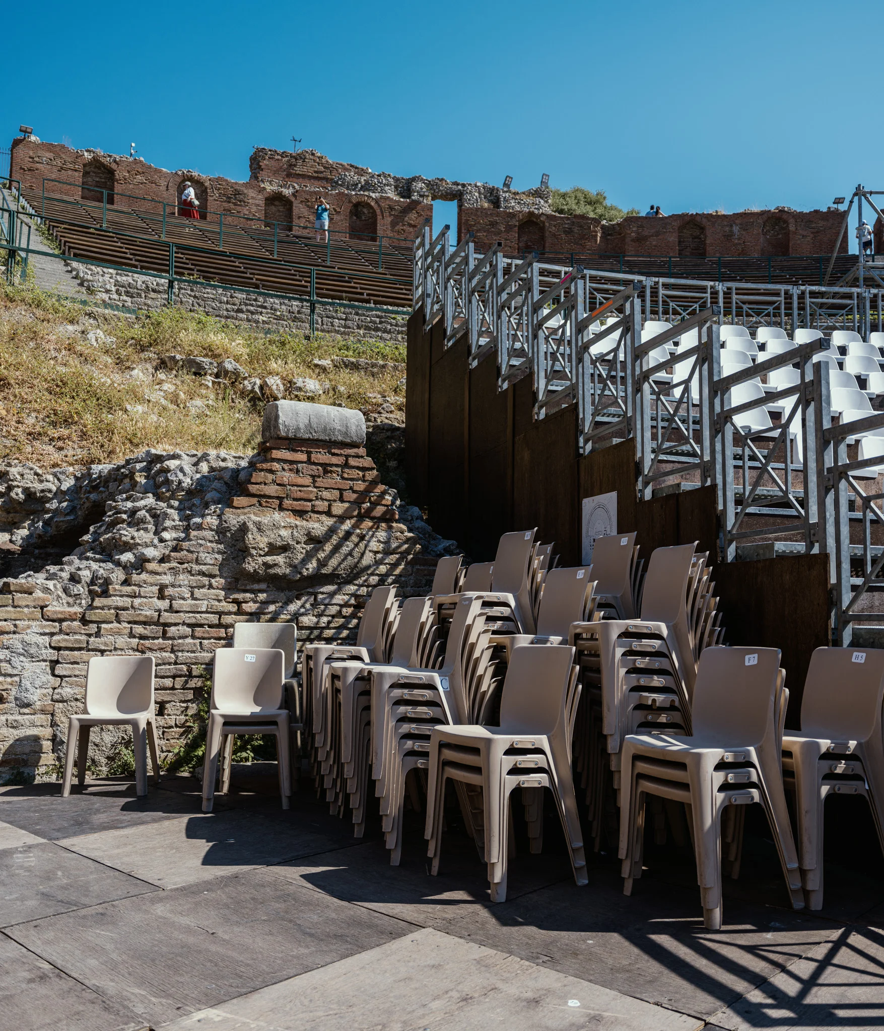 Stacked chairs in front of ancient stone ruins under a clear blue sky.