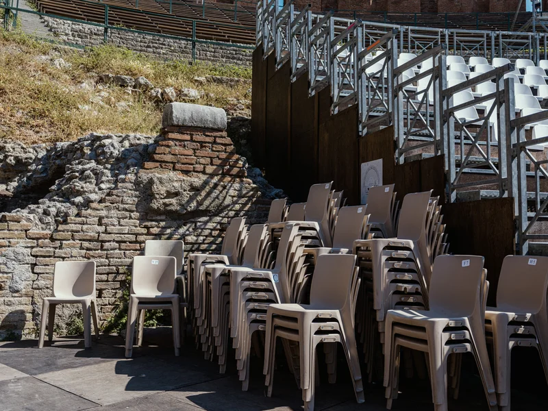 Stacked chairs in front of ancient stone ruins under a clear blue sky.