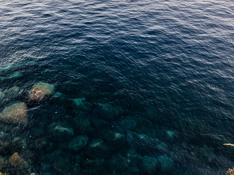 Aerial view of clear blue water with rocks visible beneath the surface.