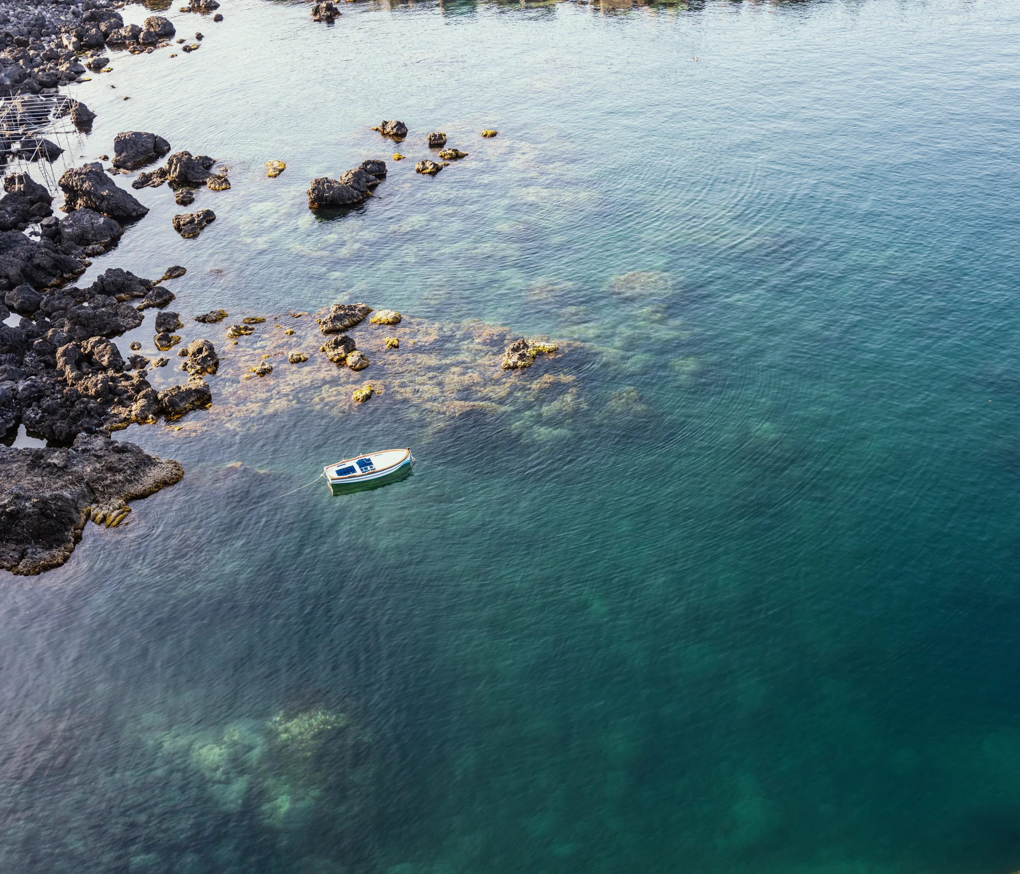 A small boat floating on clear blue-green water surrounded by dark rocks.