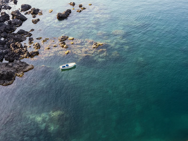 A small boat floating on clear blue-green water surrounded by dark rocks.