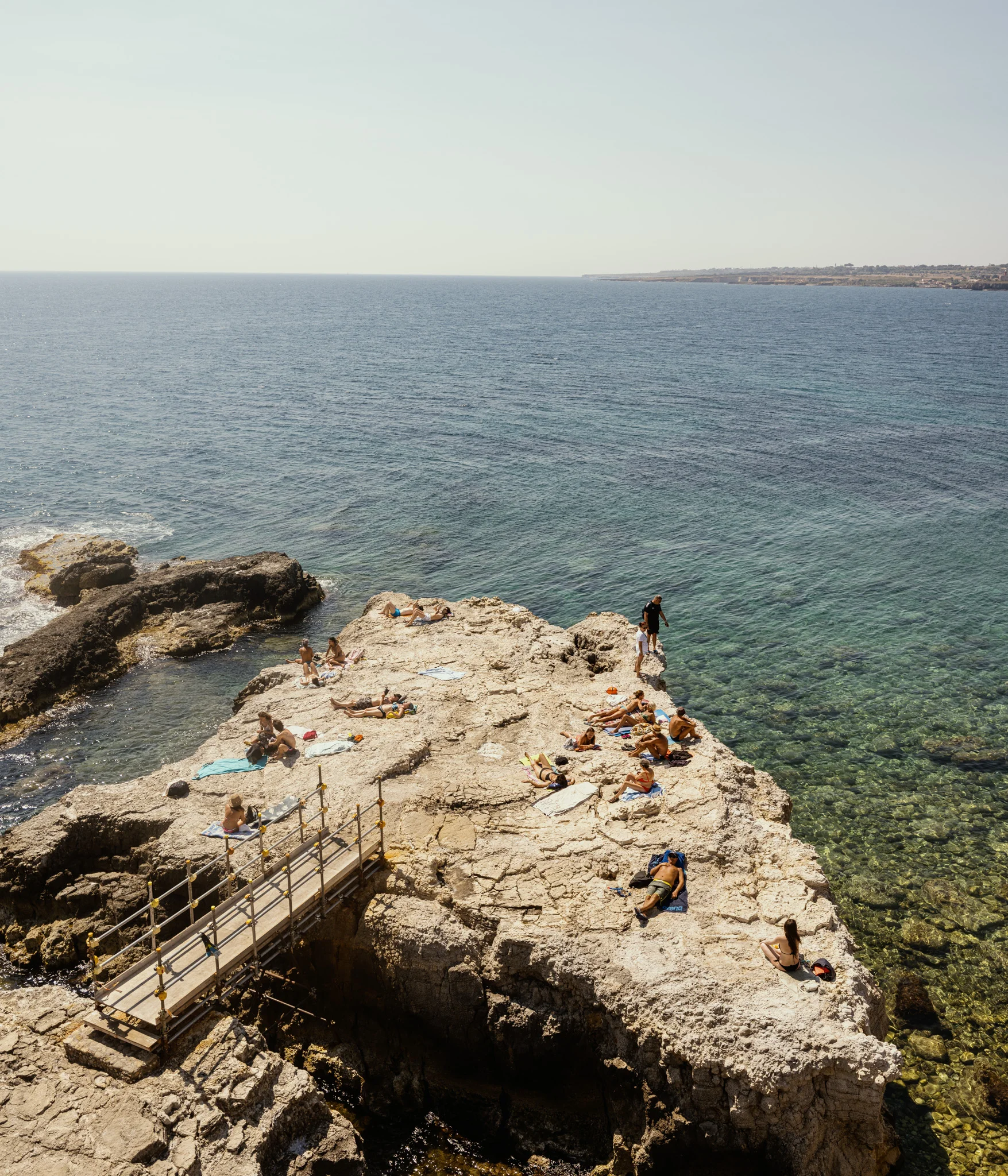 People sunbathing on a rocky outcrop by the sea.