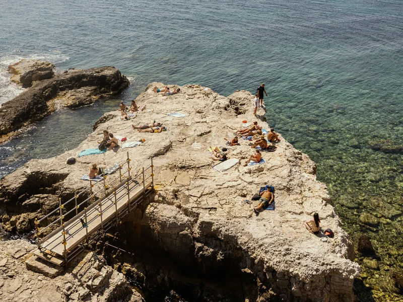 People sunbathing on a rocky outcrop by the sea.