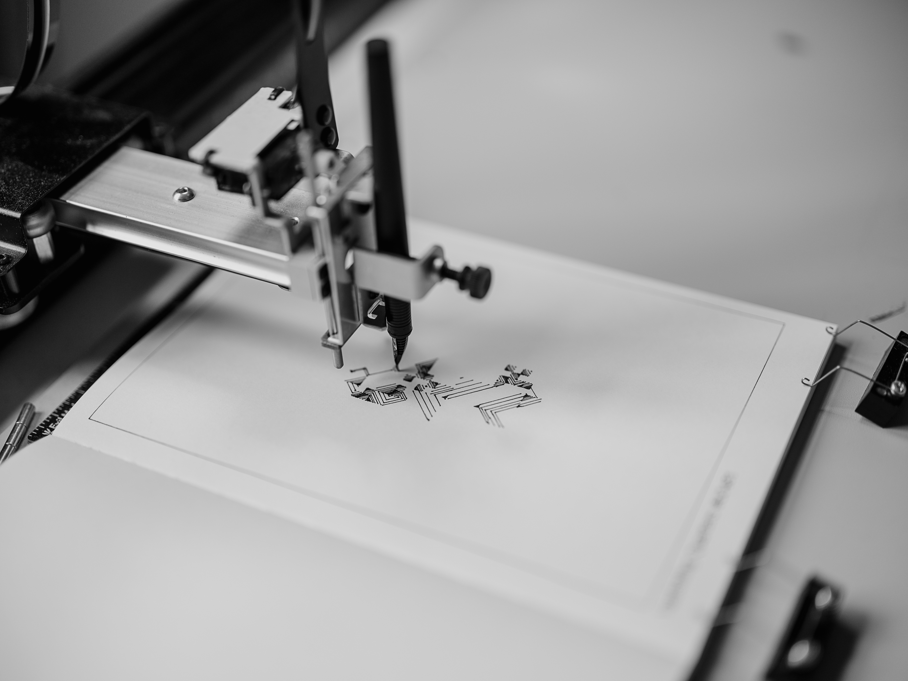 The AxiDraw pen carriage in the middle of a plot, drawing small geometric shapes onto cream Japanese paper